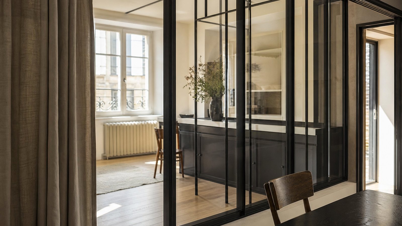 Verrière d'atelier en acier noir séparant une cuisine contemporaine d'un séjour lumineux et épuré